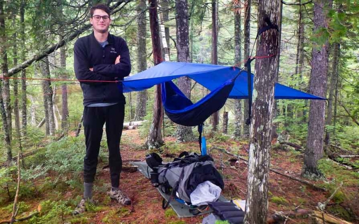 a person stands beside a shelter they made on an outward bound course in maine